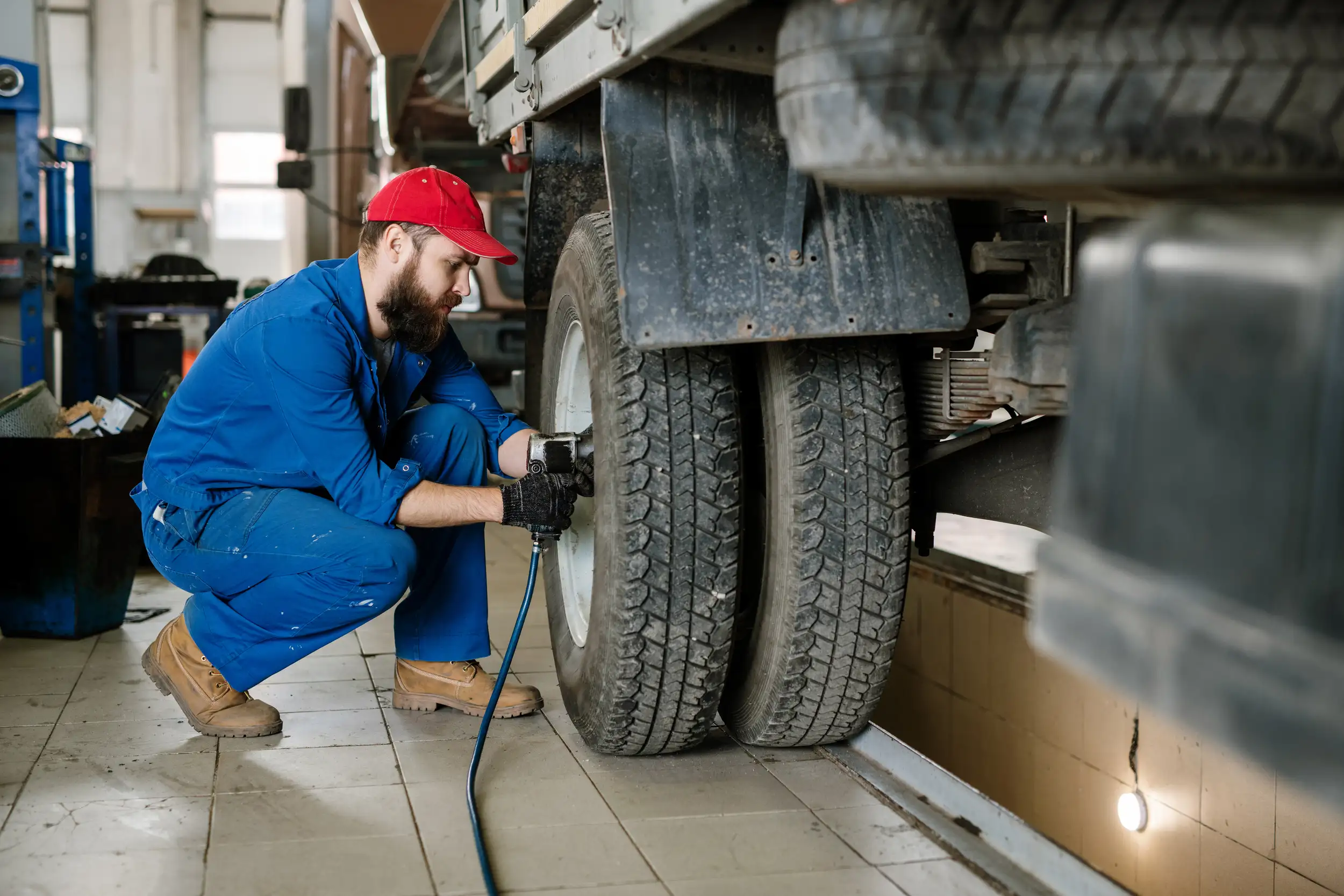 A bearded mechanic checking the tires pressure of a truck.