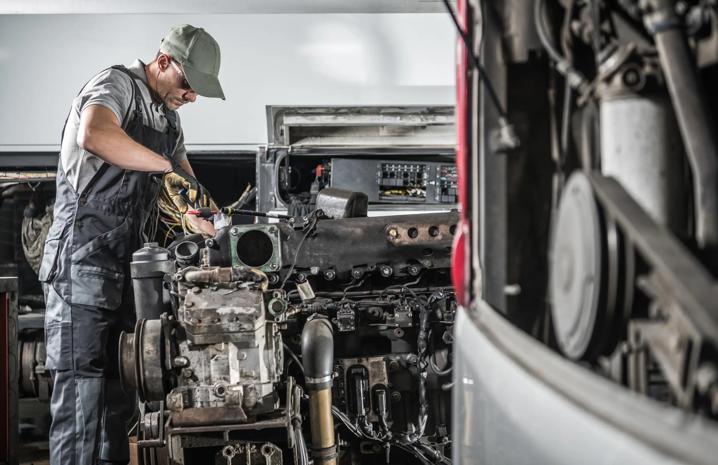 An image of a uniformed mechanic fixing the wirings and checking the parts from a trailer truck.