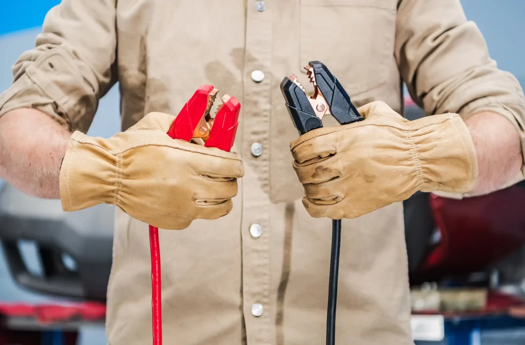 Mechanic holding red and black jumper cables, essential tools for performing jumpstarts on vehicles with dead batteries.