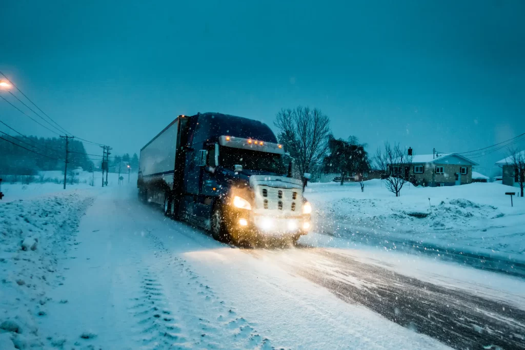 Truck driving through snow, highlighting cold weather conditions that increase the need for jumpstarts.