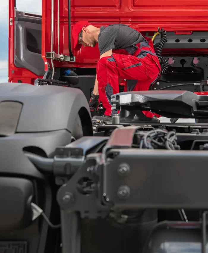 A mechanic in red uniform fixing a wirings of the trailer truck.